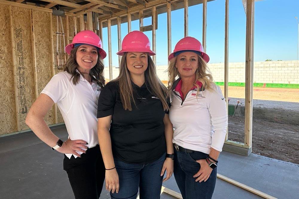 Three women in pink hard hats standing inside a home under construction, representing Women in Construction Week at Taylor Morrison.