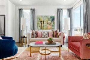 A stylish great room dressed for spring with layered textures, playful pastels, and a vibrant mix of blue, blush, and ivory furniture. Framed by large windows and soft curtains, the space radiates warmth and energy—perfect for seasonal inspiration.