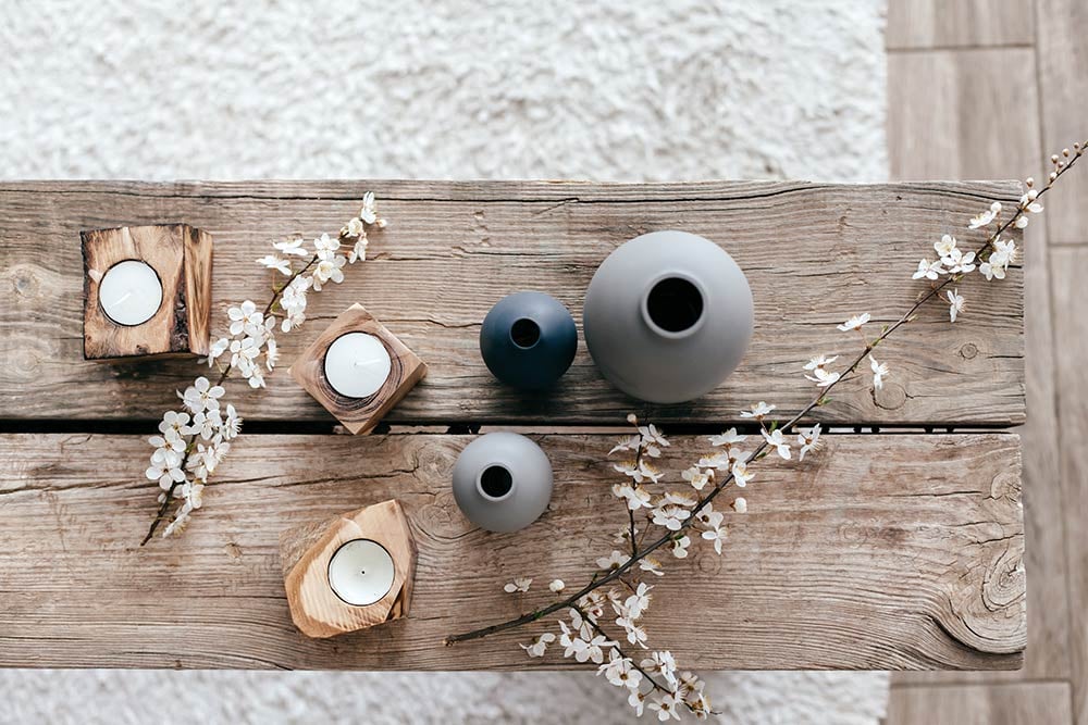 Top view of a spring-inspired vignette featuring ceramic vases, cherry blossom branches, and natural wood candle holders on a rustic table. This minimalist arrangement is perfect for seasonal styling that brings warmth and serenity into your space.