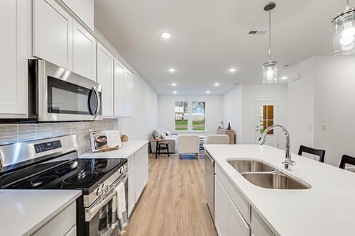 Open layout kitchen in Colonnade Townhomes, featuring white cabinetry, modern fixtures, and stainless steel appliances